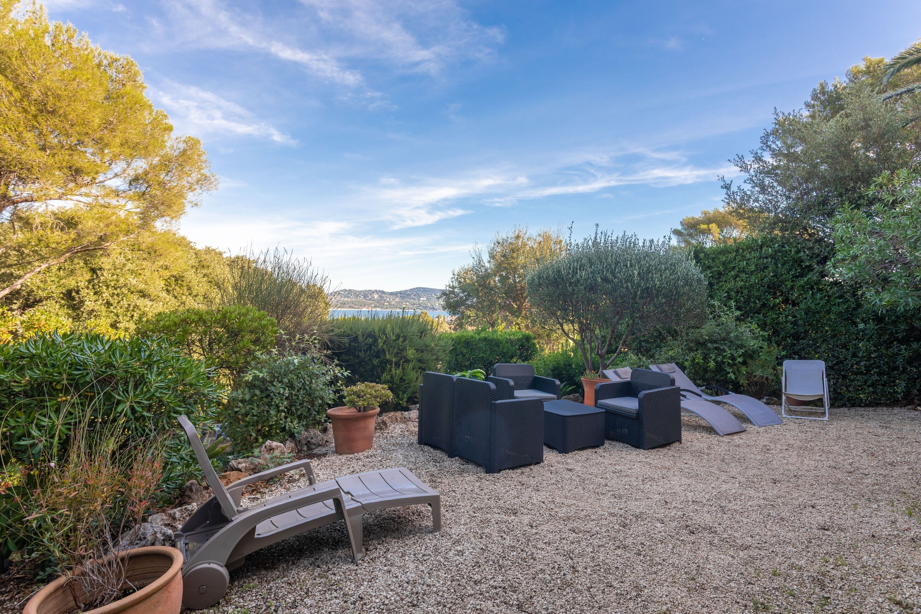 An outdoor seating area with multiple lounge chairs and a small table, surrounded by gravel and potted plants.