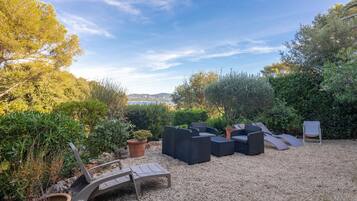 An outdoor seating area with multiple lounge chairs and a small table, surrounded by gravel and potted plants.