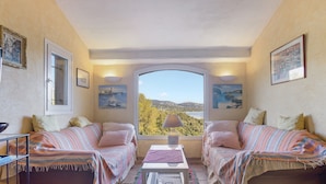 A cozy room with two beds, a small table, and a window offering a scenic view. - Villa 'La Mignonette' with Sea View, Private Garden and Wi-Fi (Cavalaire-sur-Mer)