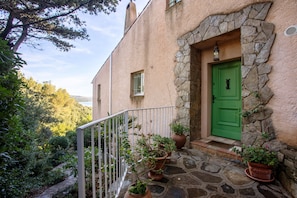 Un edificio de piedra con puerta verde, plantas en macetas y barandilla de balcón.