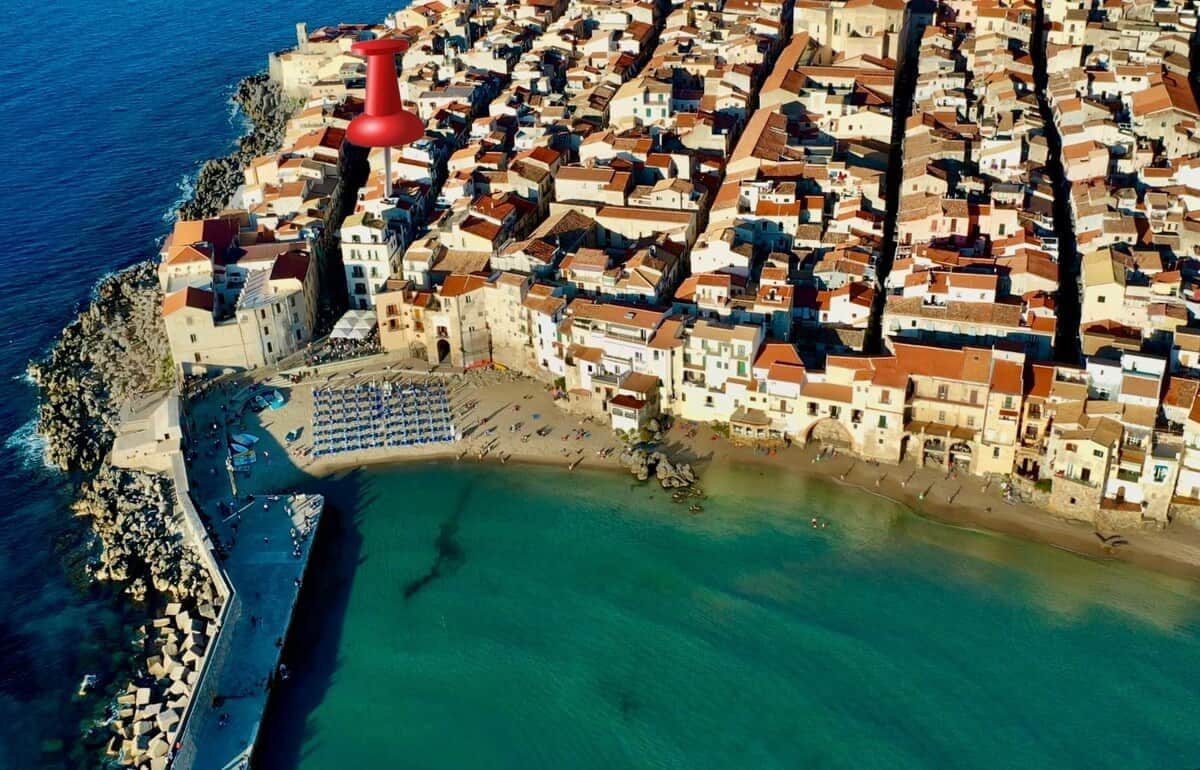 Vue aérienne d’une ville côtière avec ses bâtiments, sa plage et une structure fortifiée.