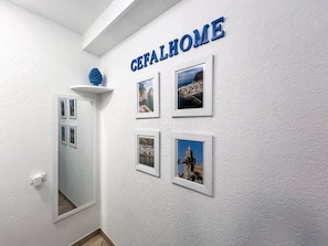 Un pasillo con una pared blanca con textura, una puerta con espejo y cuatro fotografías enmarcadas.