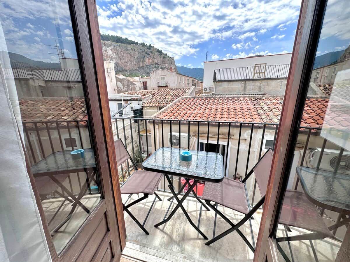 Un balcon doté d’une table et de chaises en verre, donnant sur un quartier résidentiel aux toits recouverts de tuiles rouges.