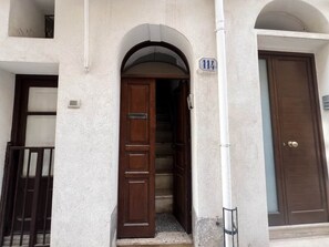 A building entrance with a wooden door, a staircase leading inside, and a mailbox on the wall.
