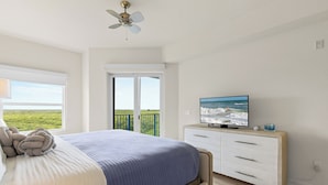 Una camera da letto con un letto, una TV su una cassettiera, un balcone con vista e una ventola a soffitto.