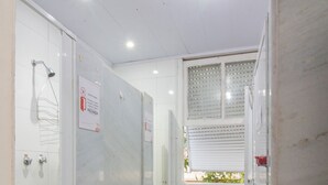 Ein schmales Badezimmer mit Fliesen, einer Dusche, einem Fenster mit Jalousien und Holzboden.