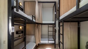Ein Schlafraum mit Etagenbetten, Holzboden, einer Stehleiter und einem kleinen Regal mit Lampe.