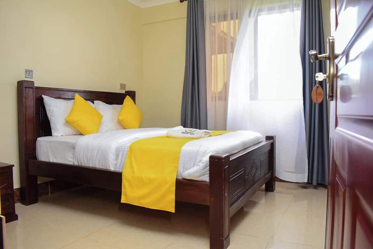 A neatly made bed with a white and yellow bedspread, two pillows, and a wooden headboard.