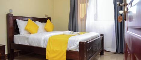 A neatly made bed with a white and yellow bedspread, two pillows, and a wooden headboard.