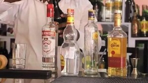 Een bartender bereidt een drankje toe met verschillende flessen alcohol op de bar.