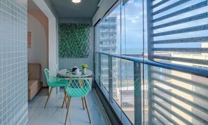 Varanda com vista para edifícios, uma mesa pequena com cadeiras e uma decoração de parede verde.