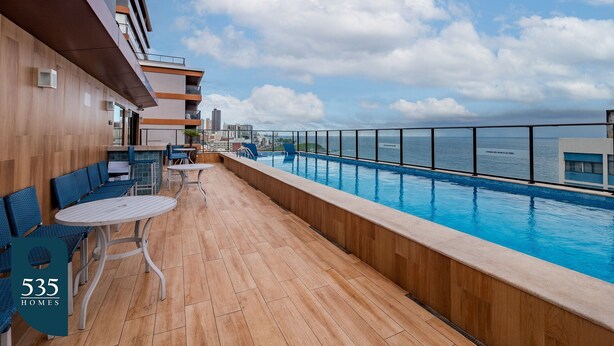 A rooftop pool area with wooden flooring, blue chairs, and tables.