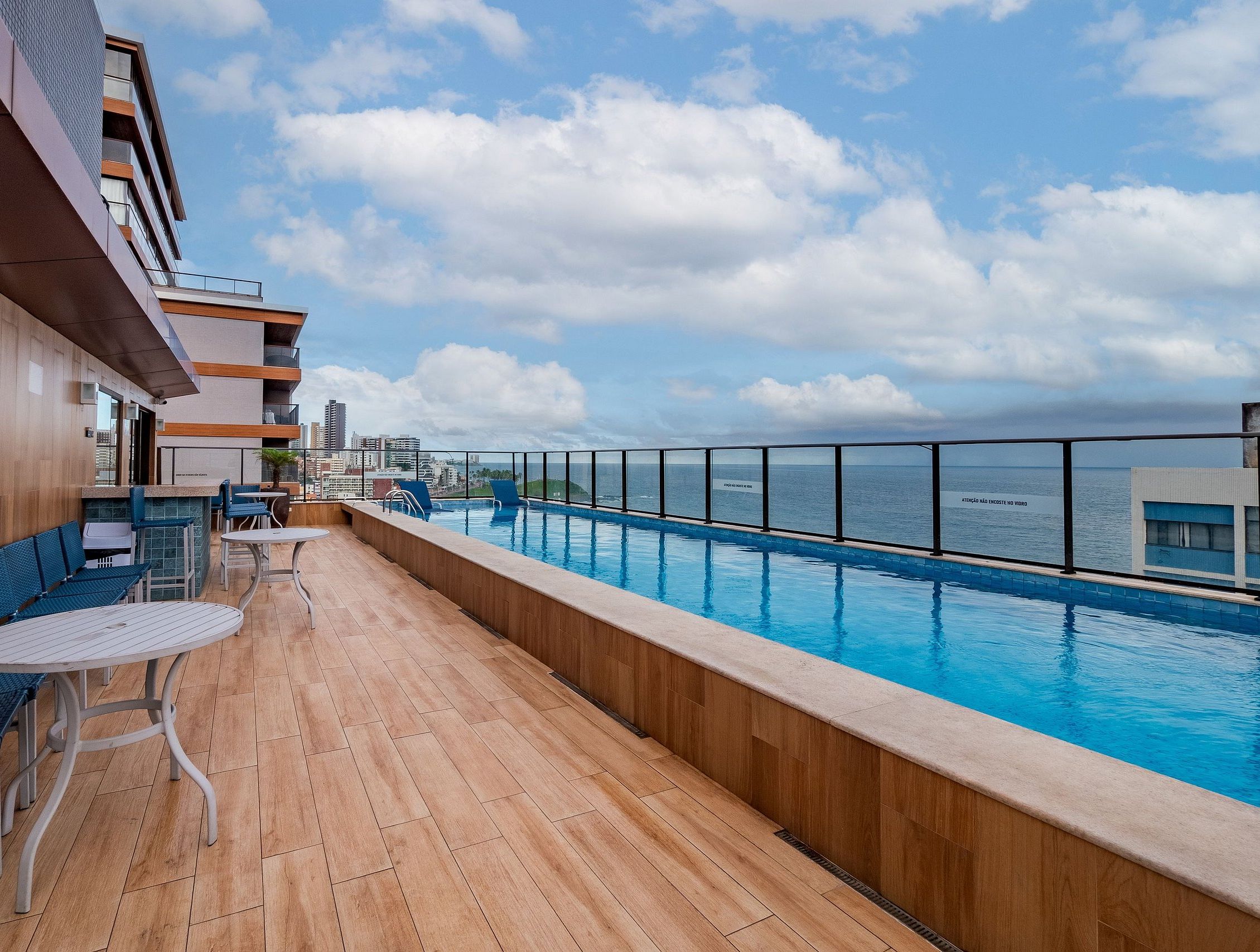 A rooftop pool area with wooden flooring, blue chairs, and tables.