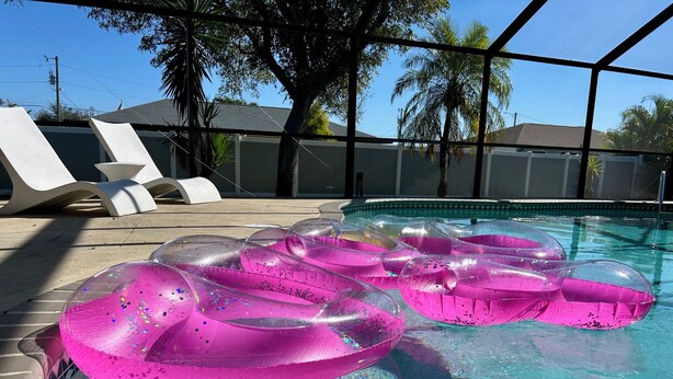 Une piscine avec des bouées roses gonflables et une eau d’un bleu cristallin.