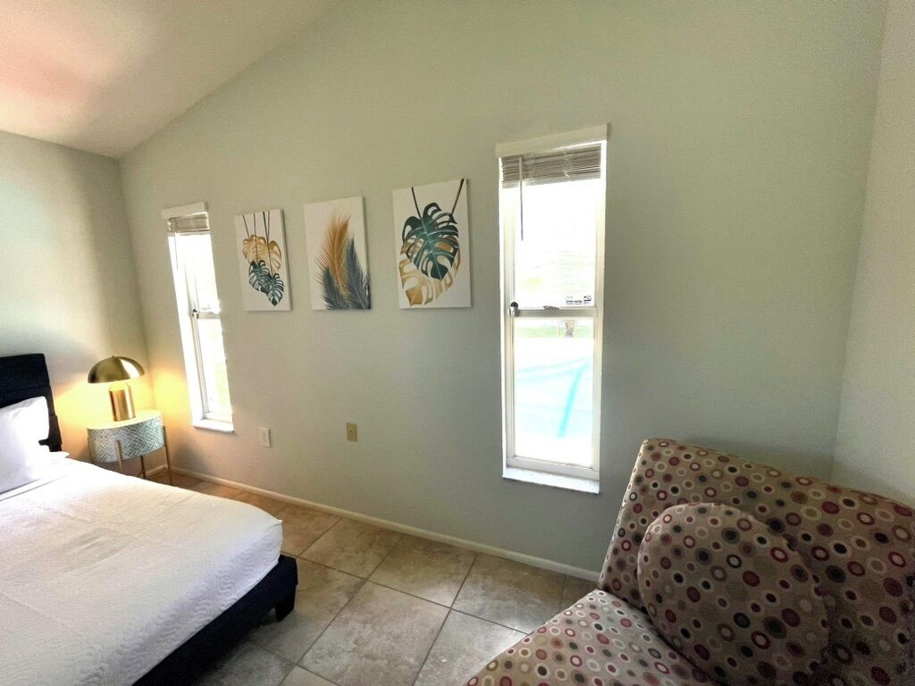 A bedroom with a bed, a nightstand, a lamp, a window, and a wall with three framed artworks.