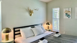 Une chambre à coucher comprenant un lit, deux tables de chevet, une décoration murale représentant une tête de cerf, et deux œuvres d’art murales.