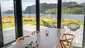 Comedor con una mesa y sillas, ventanas amplias con vista a un lago y montañas.