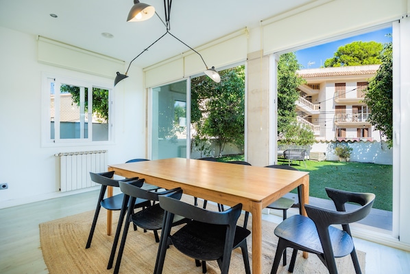 A dining area with a wooden table and black chairs, large windows, and a view of a building and greenery.