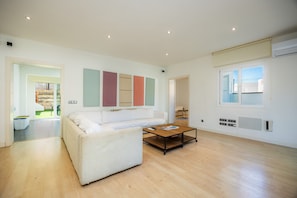 A spacious living room with a white sofa, a coffee table, and a large window.