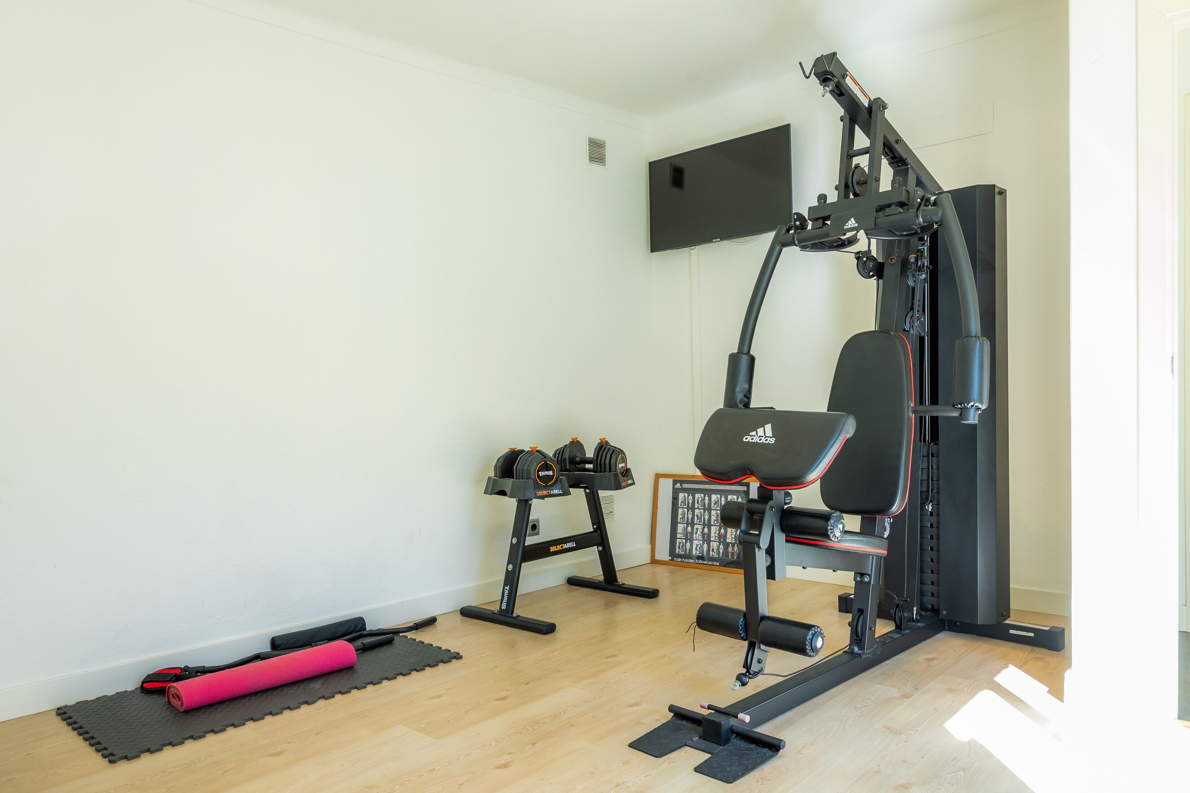 Ein Heim-Fitnessraum mit einer Langhantelbank, Kurzhanteln und einer Klimmzugstange.