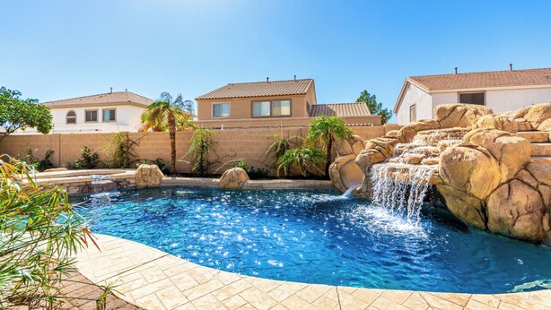 A swimming pool with a waterfall feature, surrounded by a brick wall and palm trees.