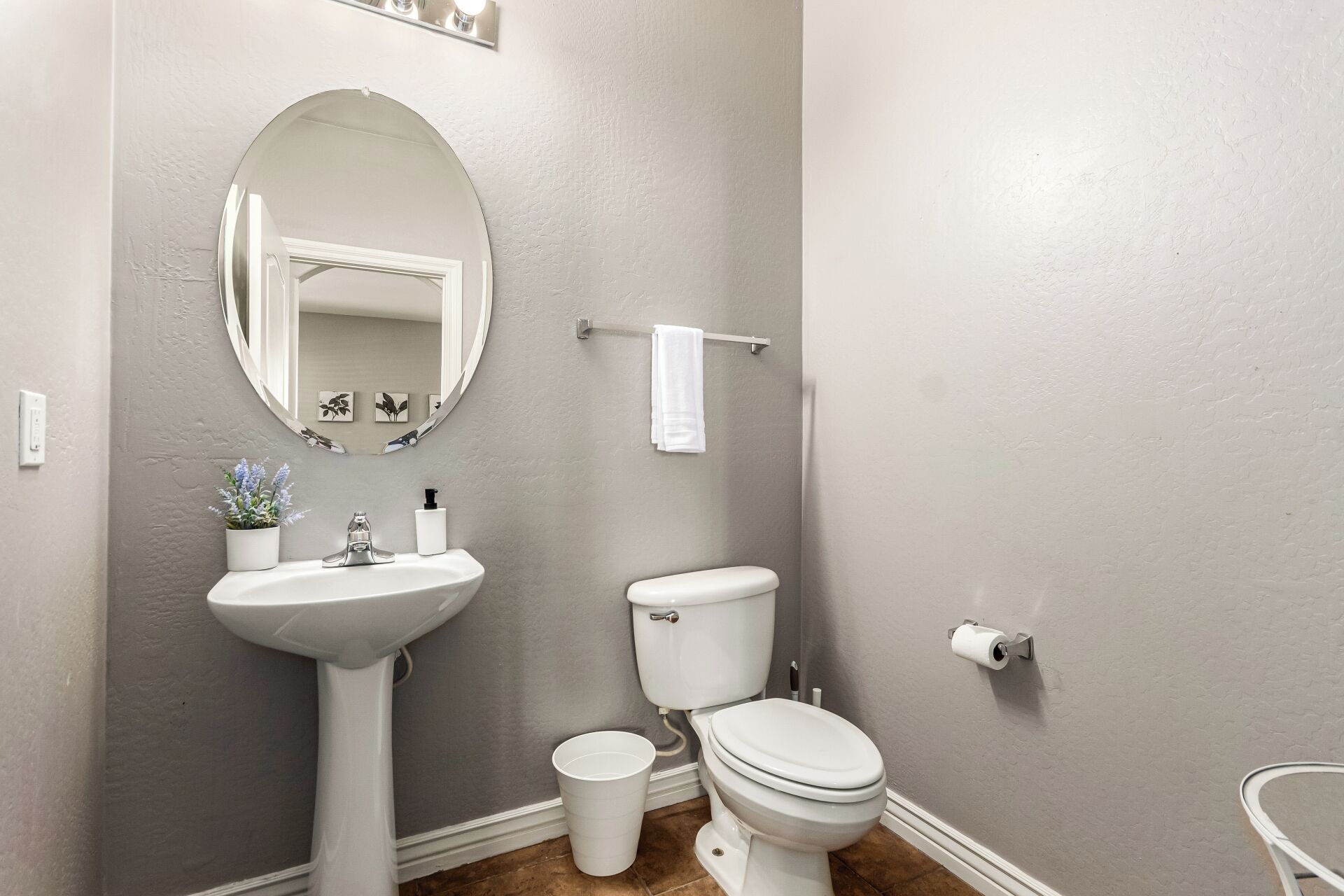 Une salle de bain avec un lavabo sur colonne, des toilettes, un miroir rond et un porte-serviettes.