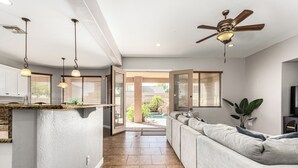 A spacious living area with a large sofa, a ceiling fan, and a view of a pool.