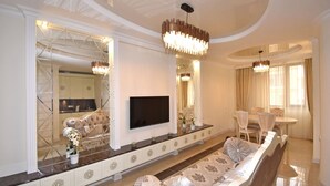 Un salón amplio con un sofá grande, un televisor montado en la pared y una zona de comedor con mesa y sillas.