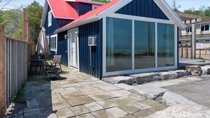 Un bâtiment bleu avec un toit rouge, de grandes fenêtres en verre et une terrasse en pierre agrémentée de mobilier d’extérieur.