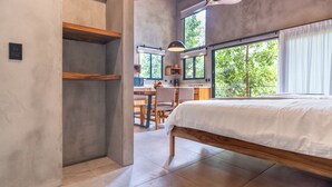 Une chambre avec un grand lit, des poutres en bois, un coin repas et une vue sur la verdure environnante.