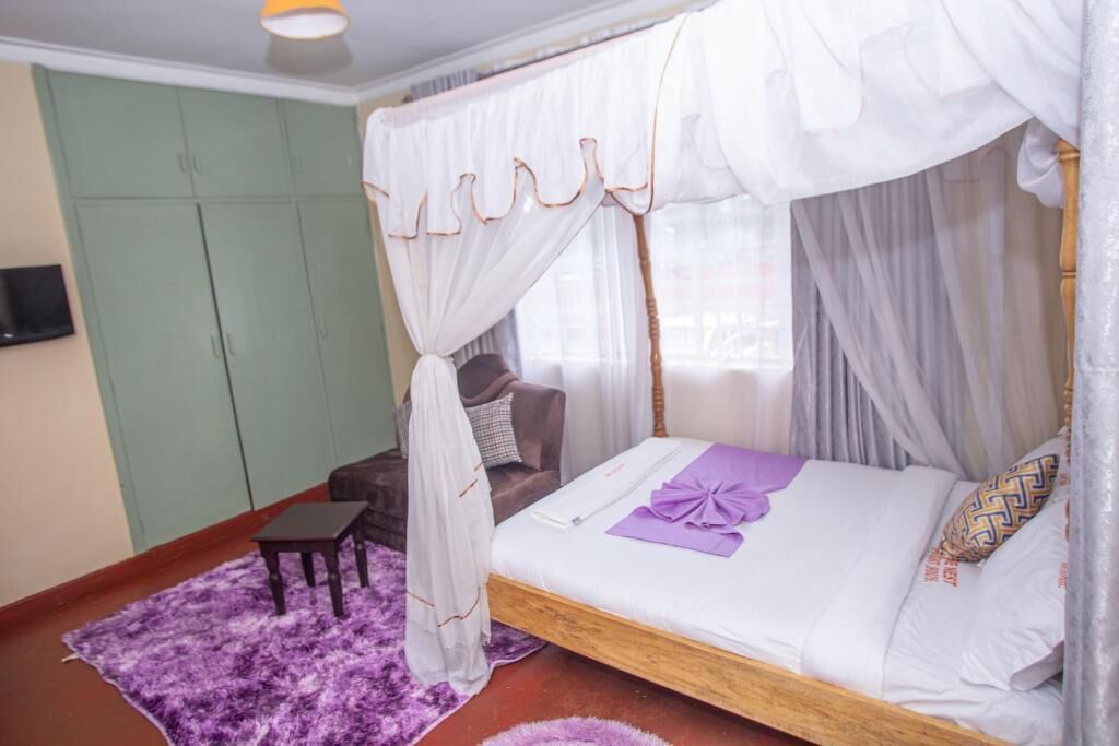 A bedroom with a four-poster bed, a small table, and a purple rug.