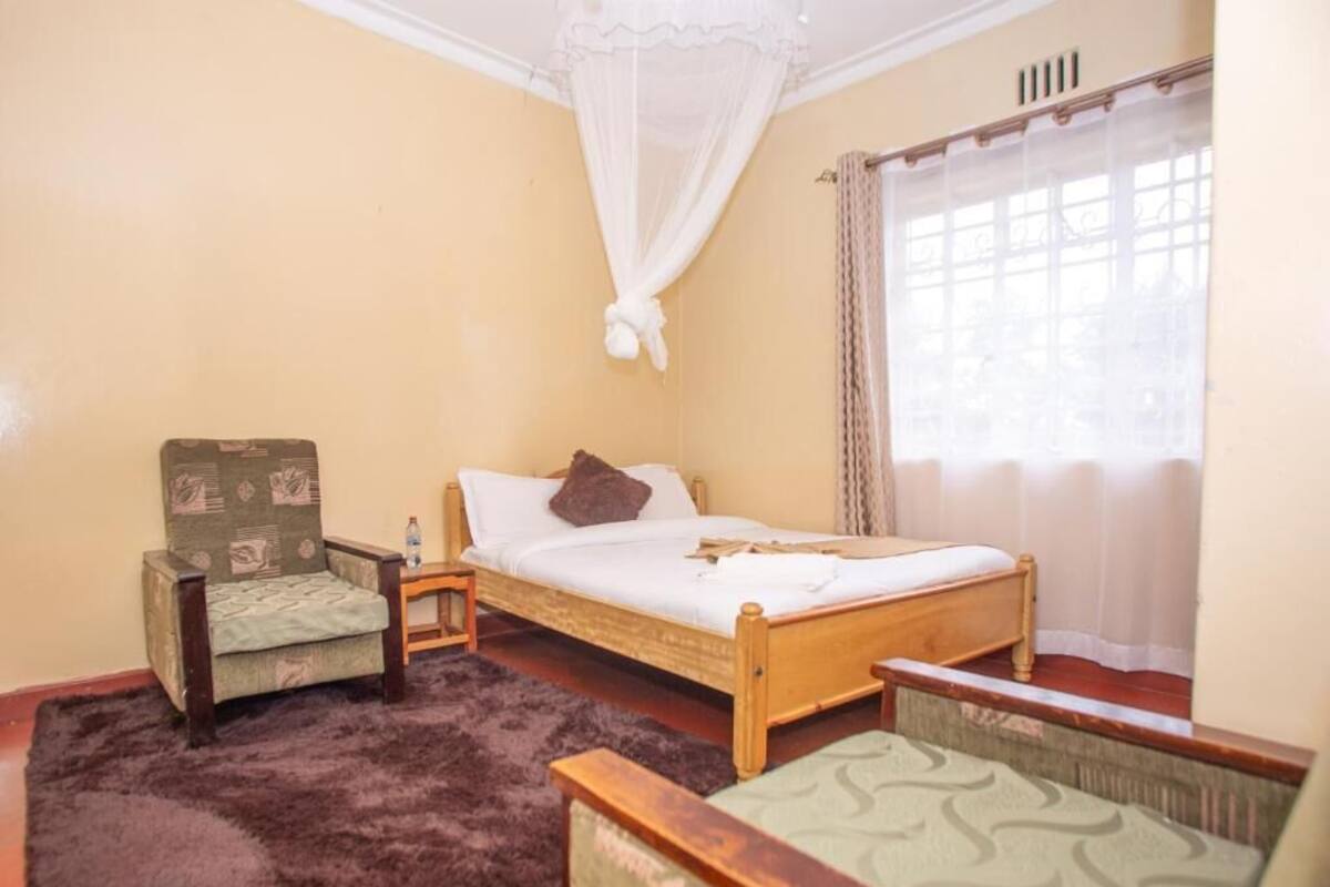 Une chambre avec un lit simple, une chaise, une table de chevet et une fenêtre avec des rideaux.