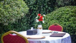 A round table with a white tablecloth, a vase with red and white flowers, a tissue box, and a book. - The Nest Guest House Kericho (Kericho)