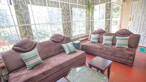 A seating area with two sofas and a small table, a decorative metal gate, and a view of greenery outside. - The Nest Guest House Kericho (Kericho)