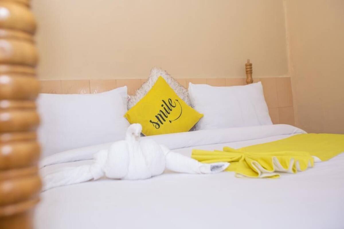 Un lit bien fait, avec une literie blanche, un coussin jaune sur lequel est écrit le mot « sourire », et un coussin blanc en forme de cygne.