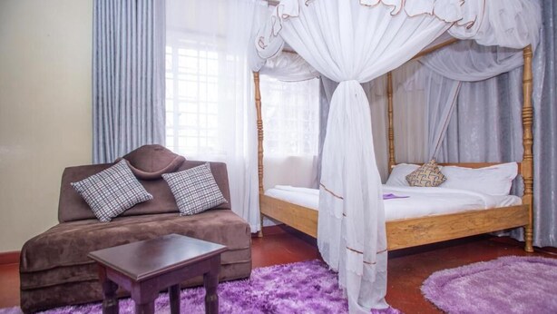 A bedroom with a four-poster bed, a sofa with cushions, a small table, and a purple rug. - The Nest Guest House Kericho (Kericho)