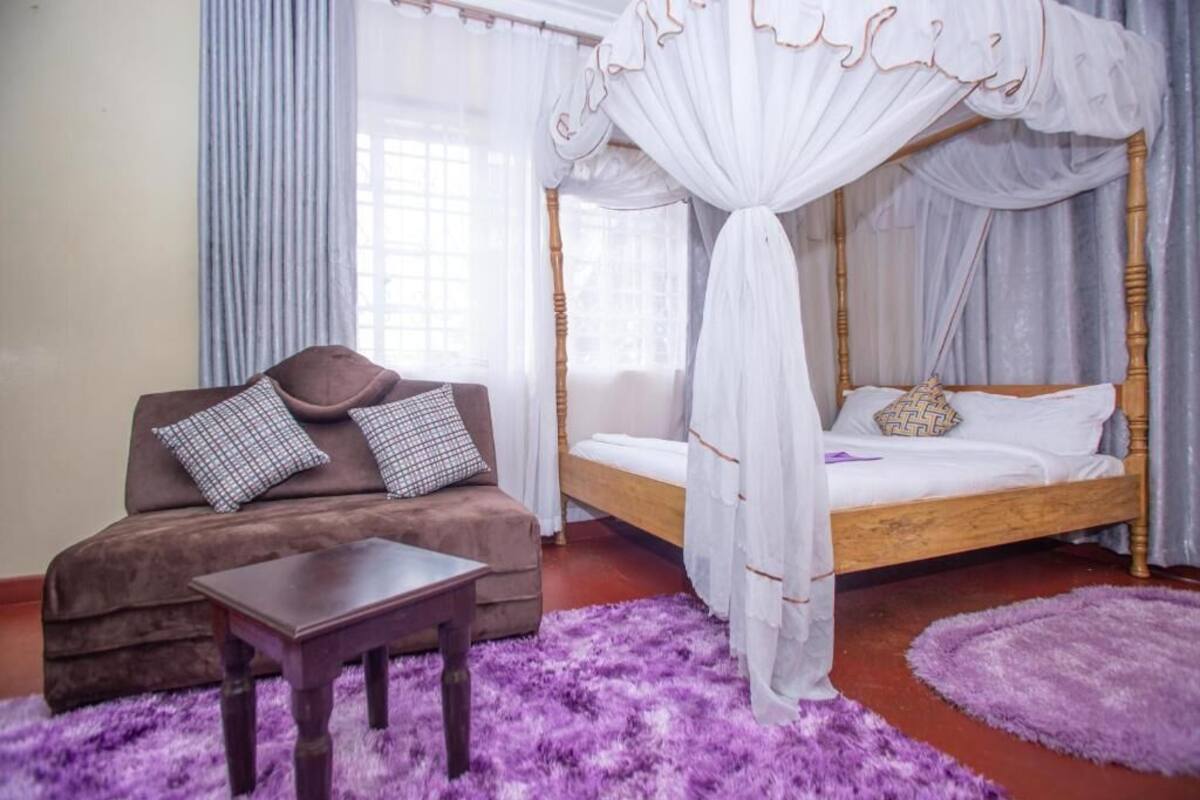 Une chambre à coucher avec un lit à baldaquin, un canapé avec des coussins, une petite table et un tapis violet.