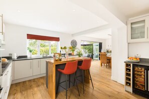 A modern kitchen with a central island, bar stools, and a wine cooler. - Blossom Tree Cottage | Garden | Parking - Pass the Keys (Bourton-on-the-Water)