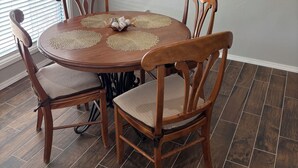 Un coin repas avec une table ronde en bois, quatre chaises, un lustre et un tableau au mur.