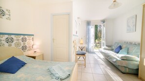 Een slaapkamer met een bed, een stoel, een bank, een tafel met een lamp, en een deur die leidt naar een balkon.