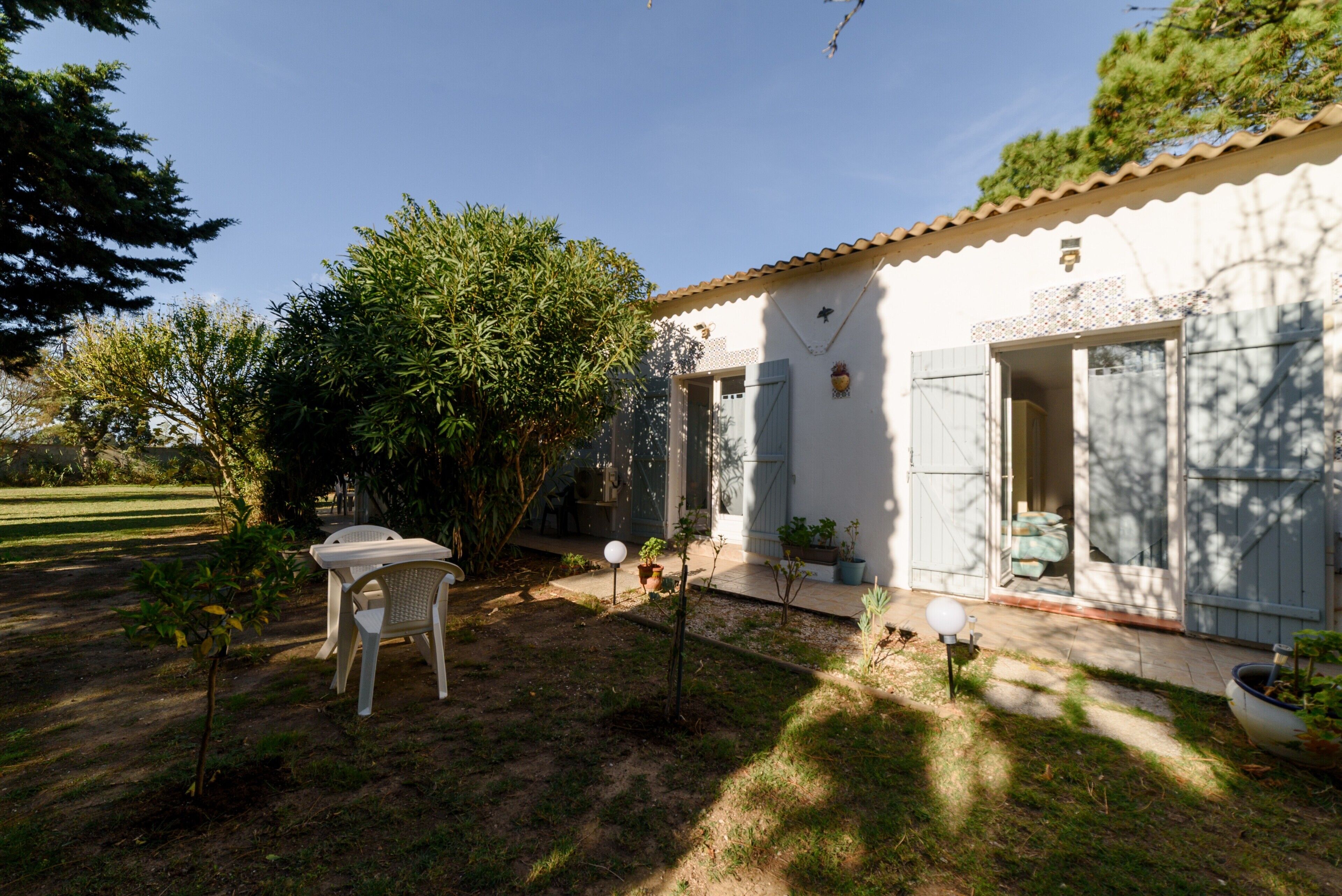Une maison blanche avec un toit en tuiles, un petit jardin avec une table et une chaise, et une porte donnant sur un porche abrité.