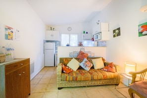 Un espacio habitable compacto con kitchenette, un sofá con cojines, un armario de madera y una silla.
