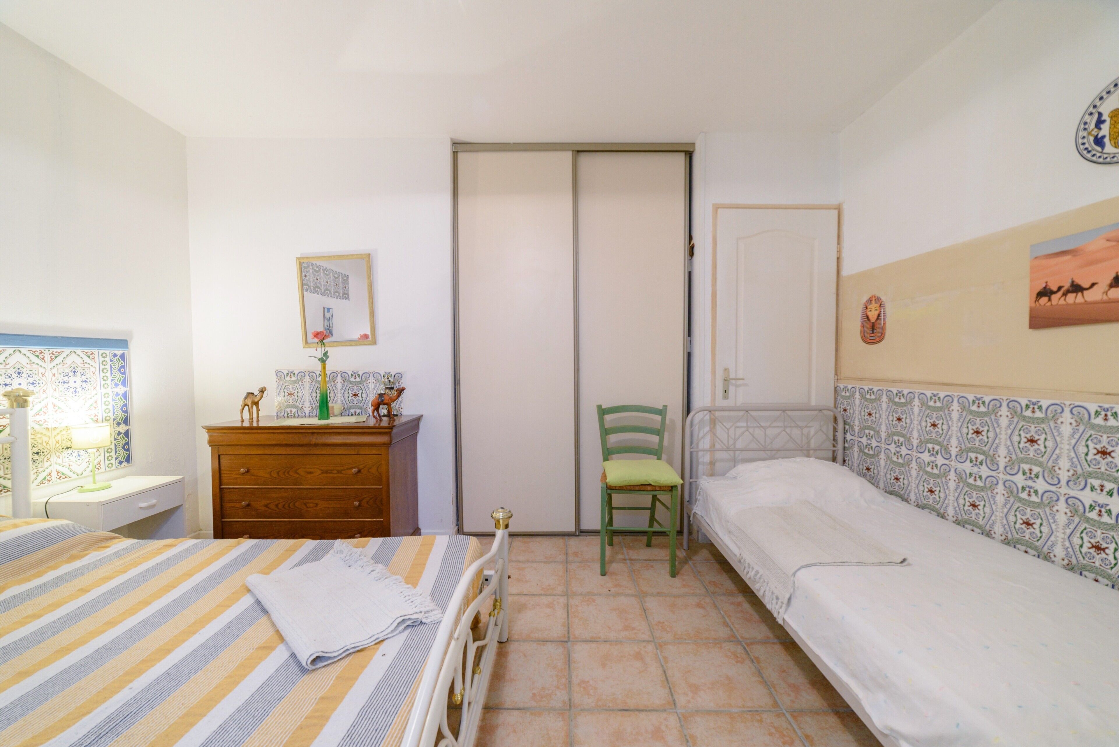 A bedroom with a bed, a chair, a dresser, a mirror, and a door.