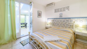 A bedroom with a bed, a nightstand, a window with curtains, a wall-mounted air conditioner, and a decorative tile border.