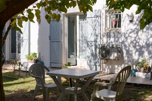 Une terrasse avec une table et des chaises, une porte, une fenêtre ornée de plantes et un ventilateur fixé au mur.