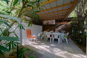 Une terrasse extérieure avec une table et des chaises, entourée de plantes en pot et d’une clôture en bois.