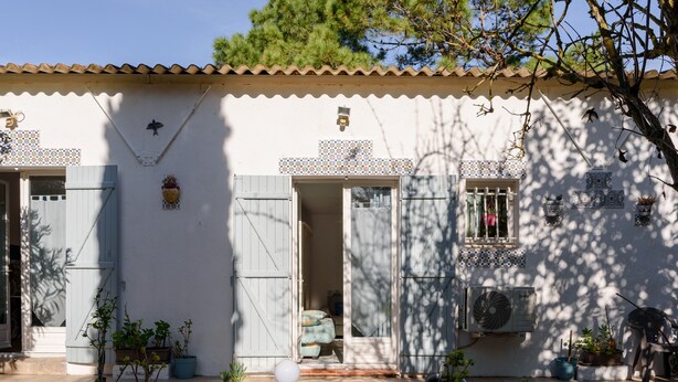 A white building with a tiled roof, a small garden with potted plants, and a door leading to an interior space.