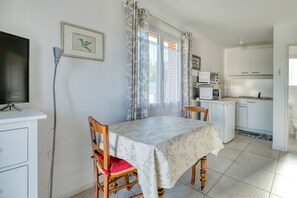 A dining area with a table, chairs, a television, and a kitchen in the background. - Studio 'Gîte Le Colibri' with Private Terrace, Garden, and Wi-Fi (La Salvetat Saint-Gilles)