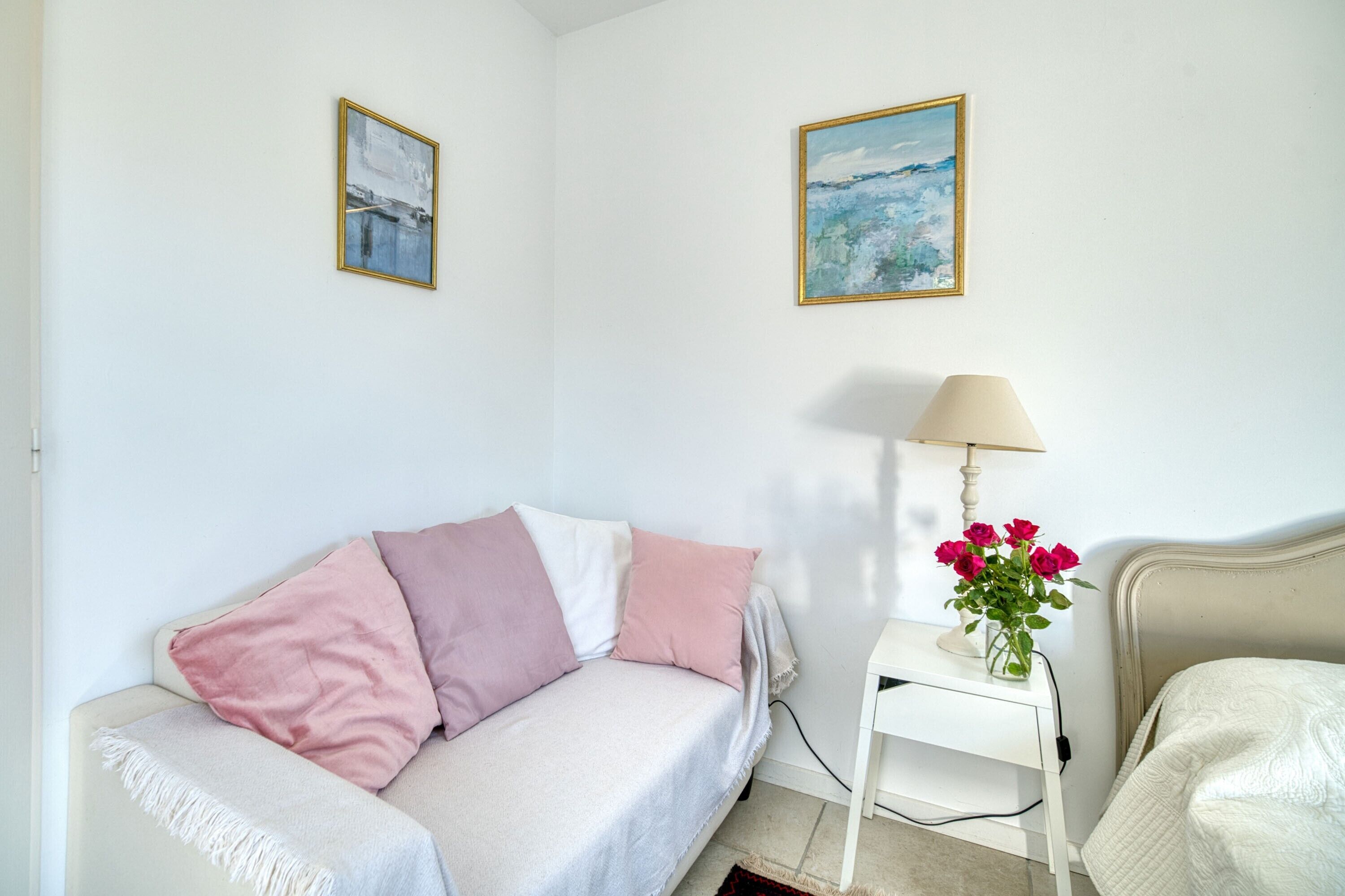Una stanza con un letto, un comodino con una lampada, un vaso con fiori e due quadri appesi al muro.