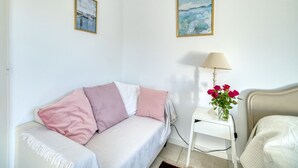 A room with a bed, a bedside table with a lamp, a vase with flowers, and two paintings on the wall.